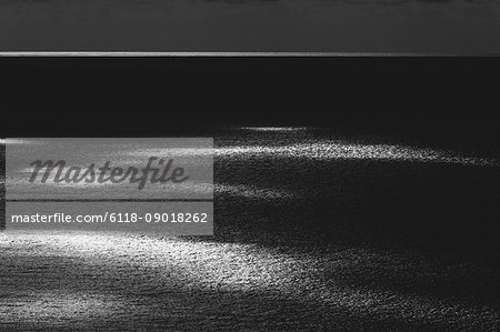 View from the land over the ocean, to the horizon in low light. Sunlight patches on the water surface. View from the land over the ocean, to the horizon in low light. Sunlight patches on the water surface.