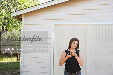 A woman holding a small fluffy chick, a baby bird in her two hands.