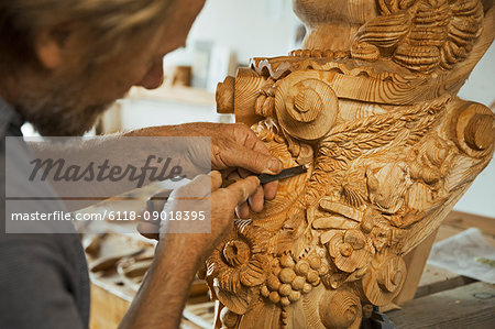 Close up of a craftsman working with a hand tool, using a small woodworking chisel on the wooden decorative features of a ship's figurehead in a workshop.