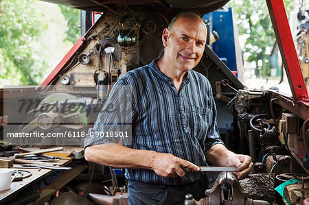 Blacksmith standing on a narrowboat barge in his workshop, holding a metal file.