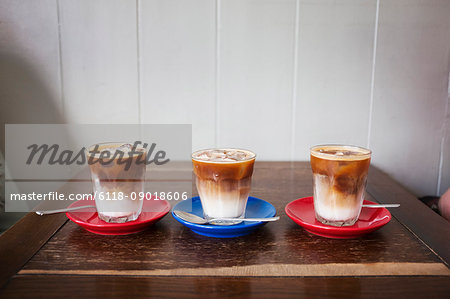 Close up of three iced coffees in glasses on a table.