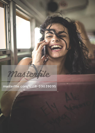 Young woman sitting on a school bus holding a mobile phone to her ear.