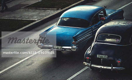 High angle shot of two classic 1950s cars driving on a road.