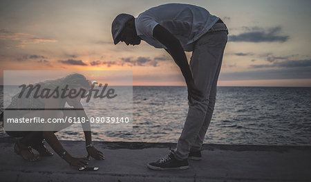 Two people looking at a phone placed on the sea wall in front of the ocean.