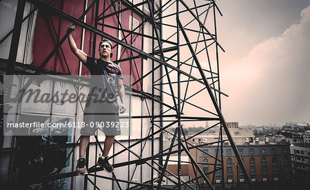 Young man standing on scaffolding on the outside of a city building.