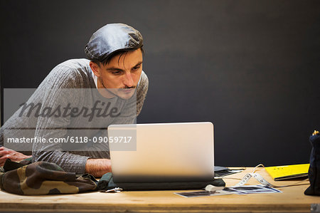 A man in a leather cap using a laptop computer.