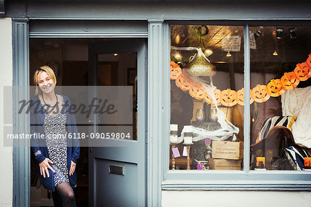 A woman standing in the doorway of her pop up interior design shop with a window display of objects.