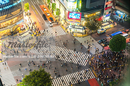 High angle view of urban street lined with illuminated buildings, pedestrians walking on pedestrian crossings.