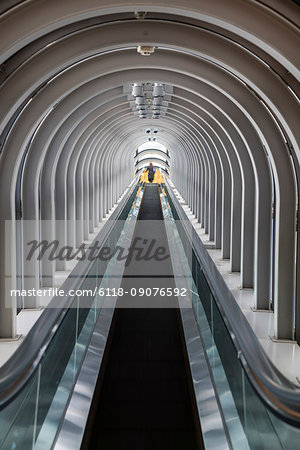 Interior view of contemporary building with escalator running across glass atrium with arched ceiling.