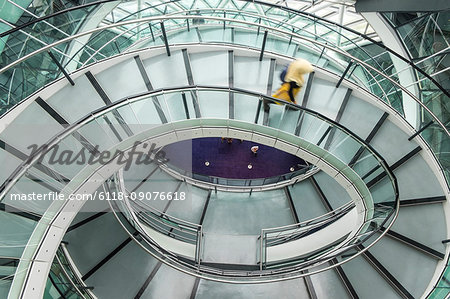 Interior view of building with person walking along glass and metal spiral staircase.