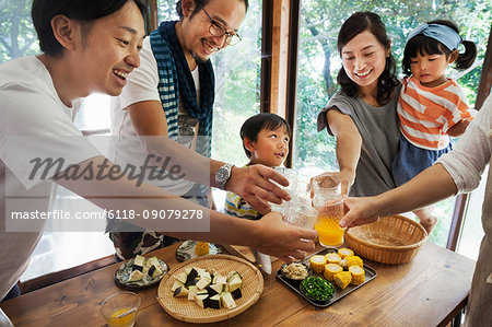 Two men, woman holding young girl and boy gathered around a table with food, holding drinking glasses, toasting.