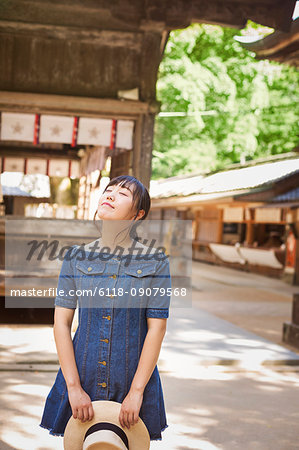 Young woman wearing blue dress and holding hat at Shinto Sakurai Shrine, Fukuoka, Japan.