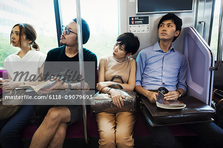 Four people sitting sidy by side on a subway train, Tokyo commuters.