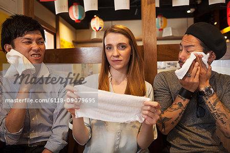 Three smiling people, woman and two men, sitting side by side at a table in a restaurant, holding wet towels.