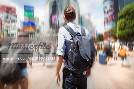 A young man with a backpack on a crowded street in downtown Tokyo.