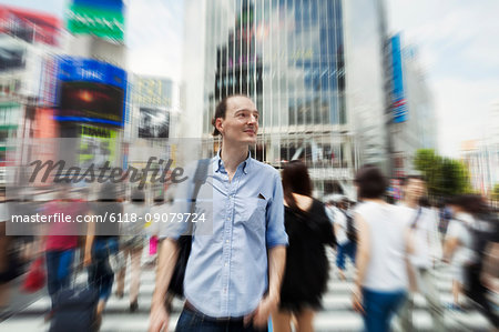 A young Caucasian man with a backpack on a crowded street in downtown Tokyo.