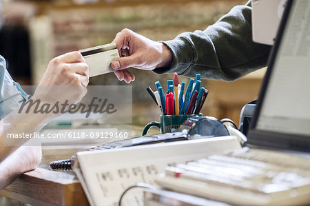 Closeup of hands exchanging  a credit card during a retail sale next to a computer at the front desk of a retail shop.