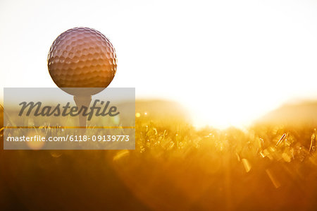 A golf ball on a tee and ready to be hit as the sun comes up.