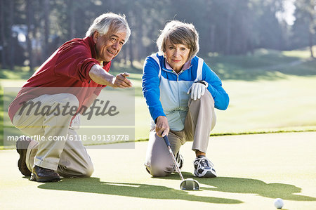 Senior couple discussing the direction of the putt on the green of a golf course.