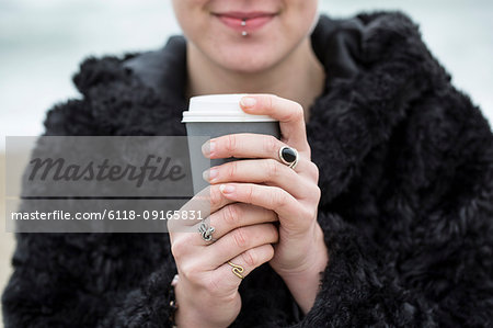 Close up of young woman wearing black furry jacket holding paper cup with hot drink.