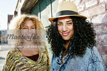 Portrait of two smiling young women with long curly black and blond hair, looking at camera.