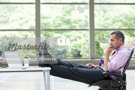 A Caucasian businessman pondering a problem at his desk with a laptop computer.