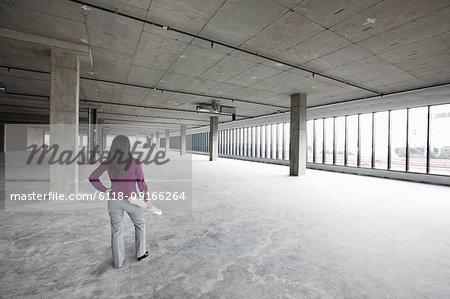 A woman architect holding architectural drawings looking out over a new raw business space.
