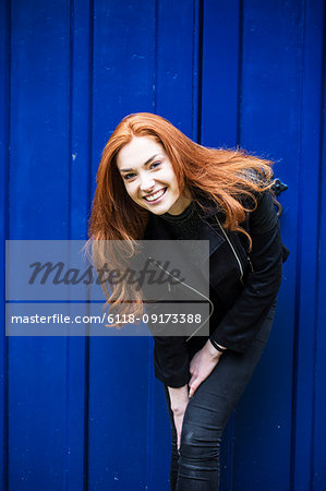 Portrait of smiling young woman with long red hair in front of bright blue door.