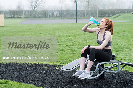 Young woman with long red hair wearing sports kit, exercising outdoors.
