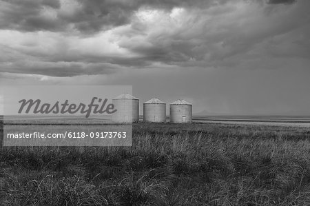 Grain silos and storm clouds over vast areas of farmland and prairie.