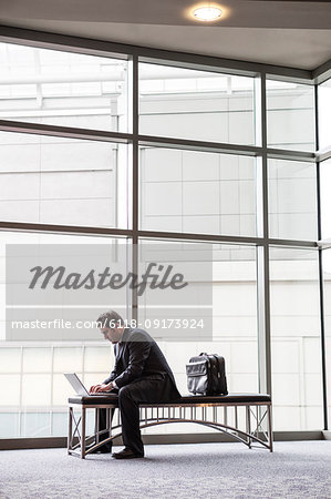 A businessman working on a laptop computer on a bench in a convention centre lobby
