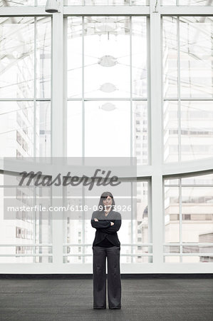 A portrait of a young businesswoman standing in front of a window in a large convention centre lobby.
