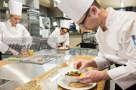 A Caucasian male chef putting the finishing touches on a plate of fish in a commercial kitchen.