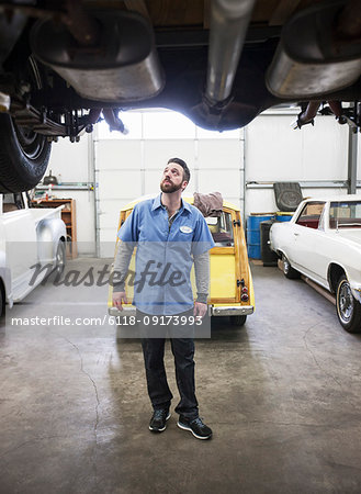 A car mechanic checking the undercarriage of an automobile he's working on in a shop.