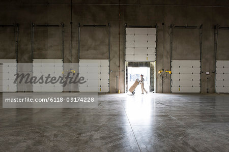 A warehouse worker with a hand truck walking past an open loading dock door in a large distribution warehouse.