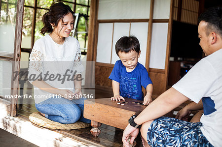 Japanese woman, man and little boy sitting on floor on porch of traditional Japanese house, playing Go.