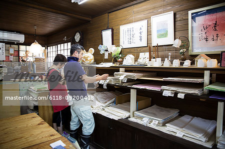 Japanese man and woman standing in a workshop with a display of washi papers and small traditional objects.