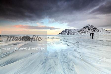 Sunset and hikers on Skagsanden beach surrounded by snow covered mountains, Flakstad, Lofoten Islands, Arctic, Norway, Scandinavia, Europe