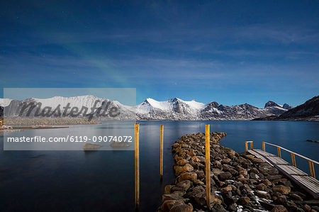 Stars of the polar night frame the frozen sea surrounded by snowy peaks, Mefjord Berg, Senja, Troms county, Norway, Scandinavia, Europe