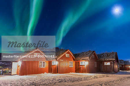 The Northern Lights (aurora borealis) and moon light up typical wood huts called Rorbu, Manndalen, Kafjord, Lyngen Alps, Troms, Norway, Scandinavia, Europe