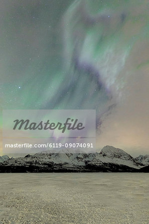 The icy lake of Jaegervatnet framed by the Northern Lights (aurora borealis) and starry sky in the polar night, Lyngen Alps, Troms, Norway, Scandinavia, Europe