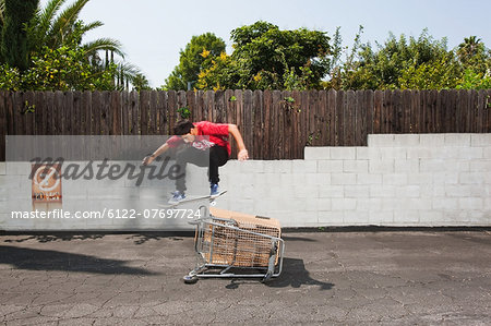Man on skateboard jumping over a shopping trolley