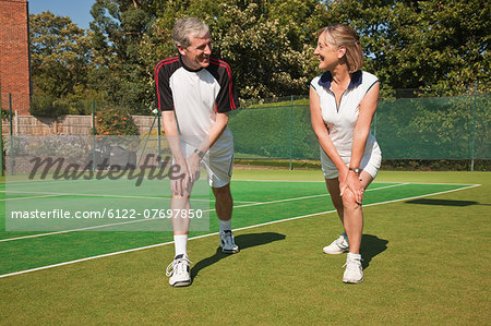 Mature woman and senior man performing warming up exercises on tennis court
