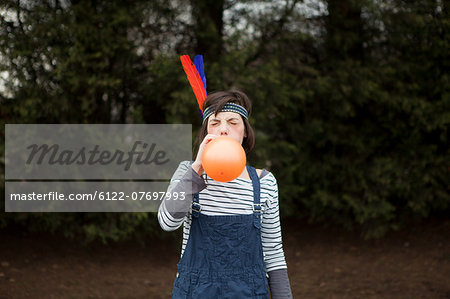 Young woman in headdress, blowing up a balloon