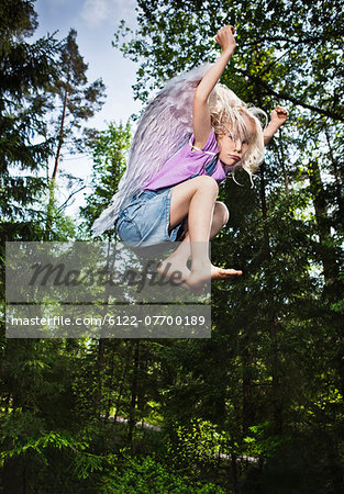 Girl wearing wings and jumping in forest