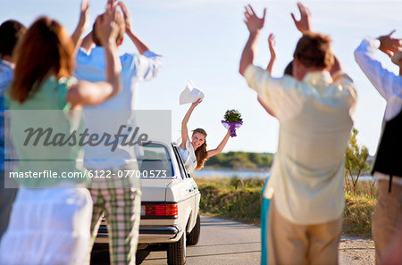 Bride waving to wedding party from car