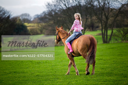 Teenage girl riding horse in field