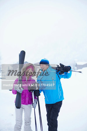 Couple carrying skis and poles in snow