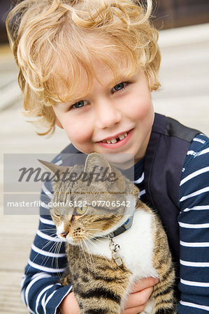 Smiling boy holding cat outdoors