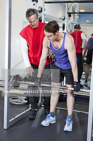 Man lifting weights with trainer in gym